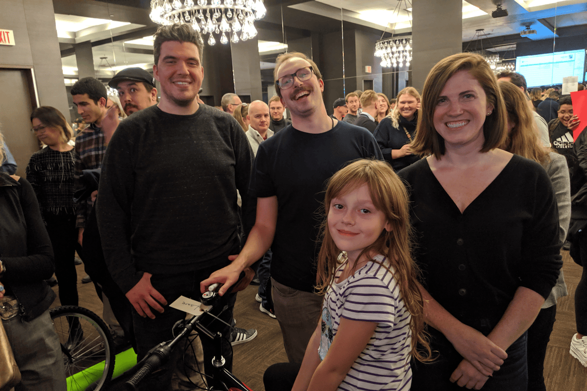 Three corporate team building participants standing with a young girl sitting on her new bicycle at a LEVEL 12 philanthropic event.